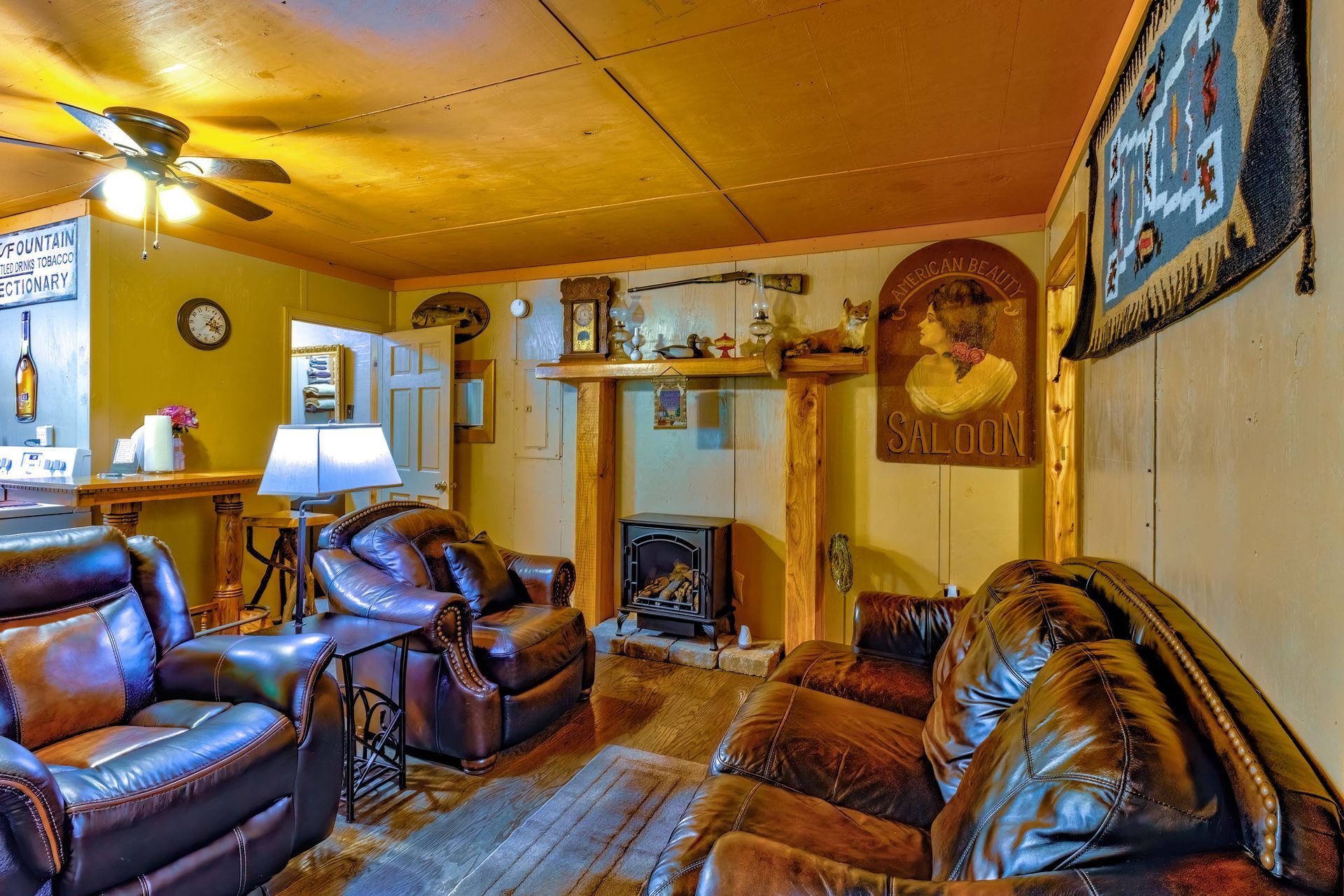 Cozy living room with brown leather sofas, warm yellow walls, lamps, and a fireplace mantel with wall art