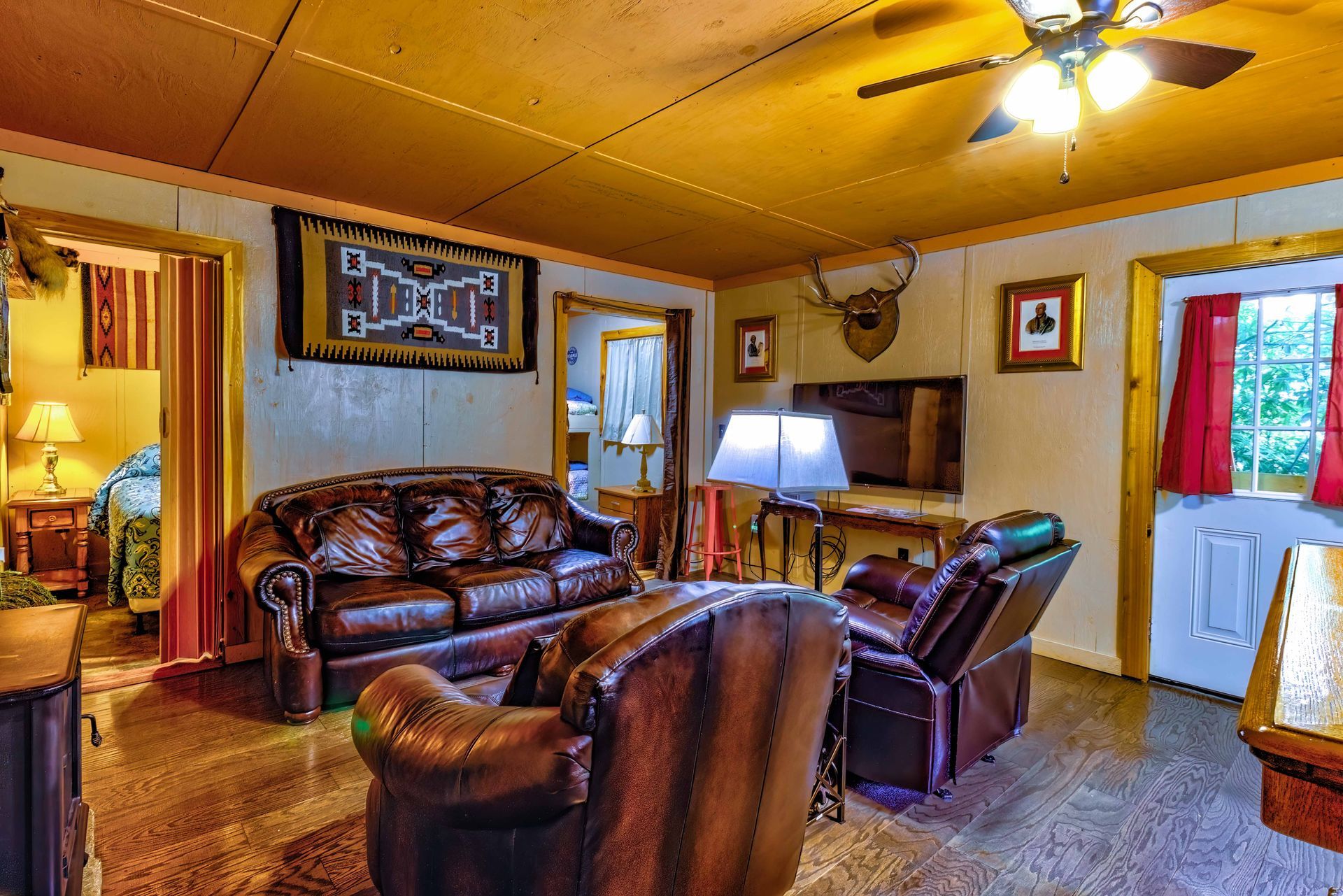 Cozy living room with leather sofas, ceiling fan, TV, lamp, and a blue door with red curtains