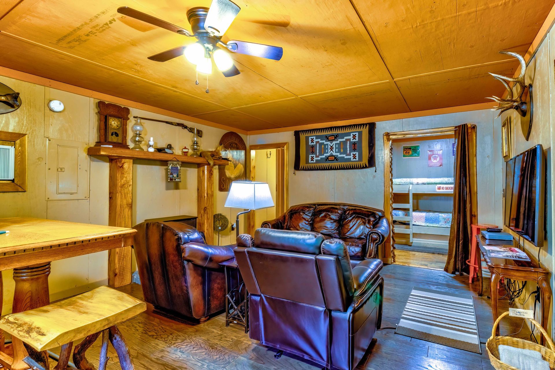 Cozy cabin living room with leather chairs, lamp, ceiling fan, and wood-paneled walls