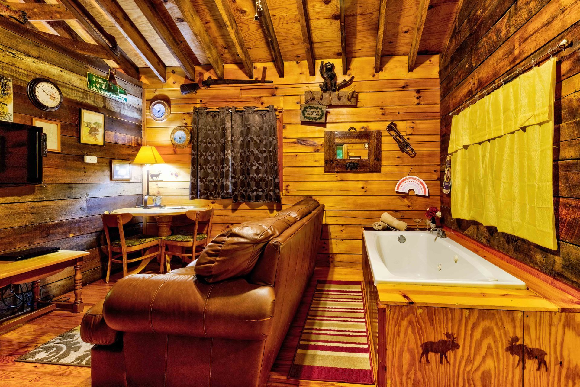 Rustic wooden cabin interior with leather sofa, desk, window, and bathtub