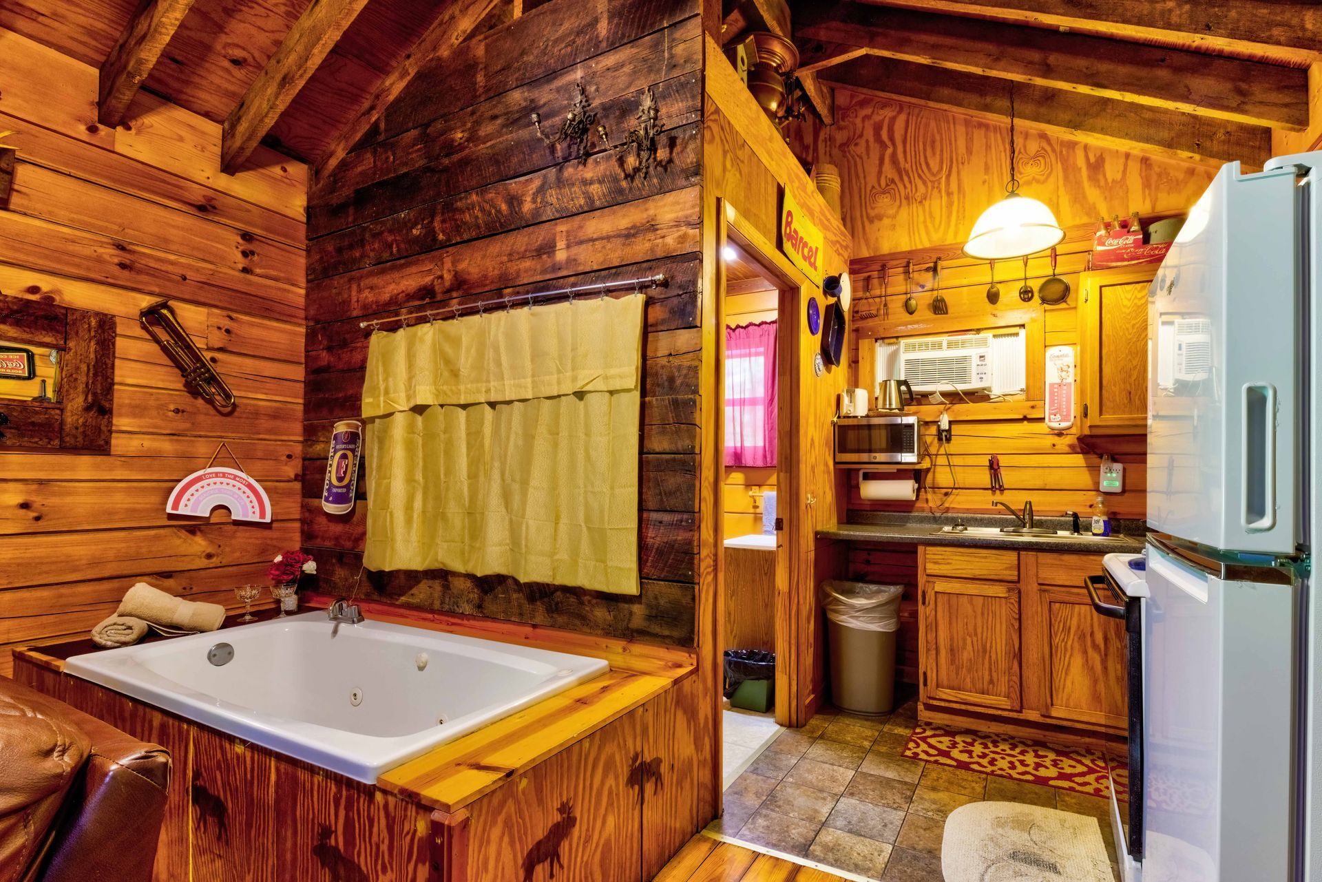Rustic log cabin bathroom with a corner bathtub, wood cabinetry, and a white refrigerator
