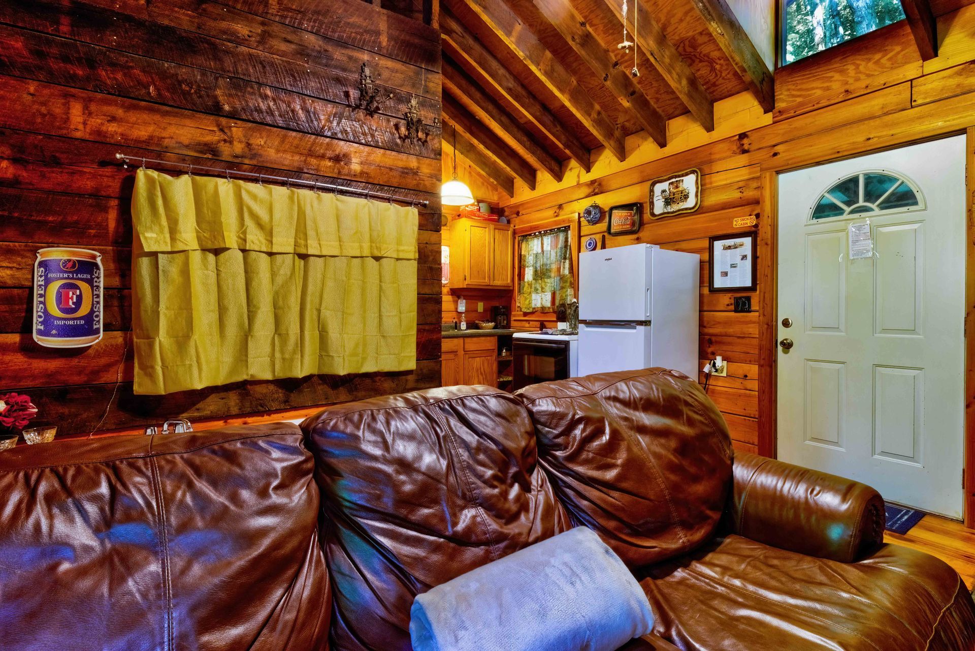 Cozy log cabin living room with leather couch, wood walls, white fridge, and white door