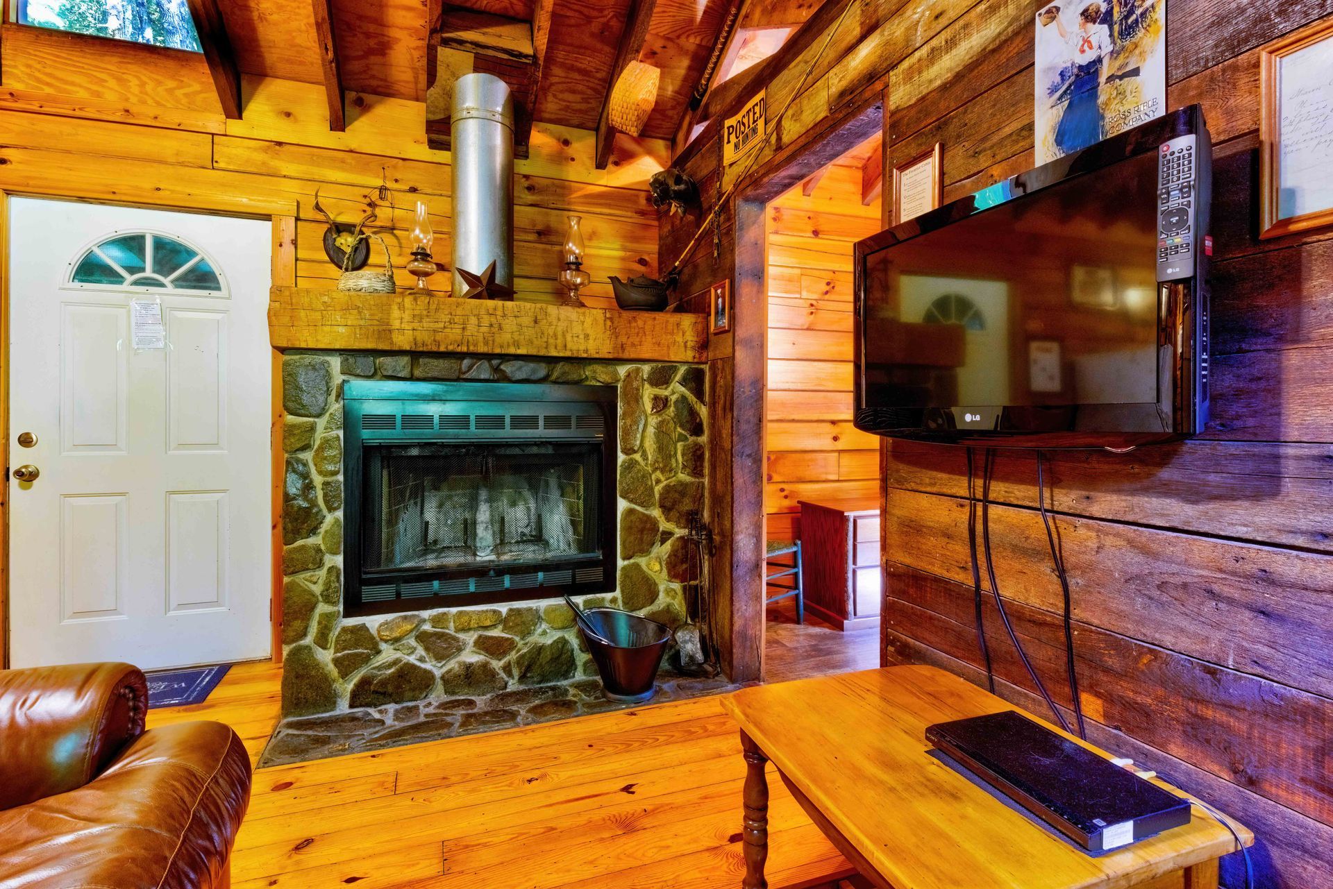 Cozy rustic living room with stone fireplace, wood walls, white door, and wall-mounted TV.
