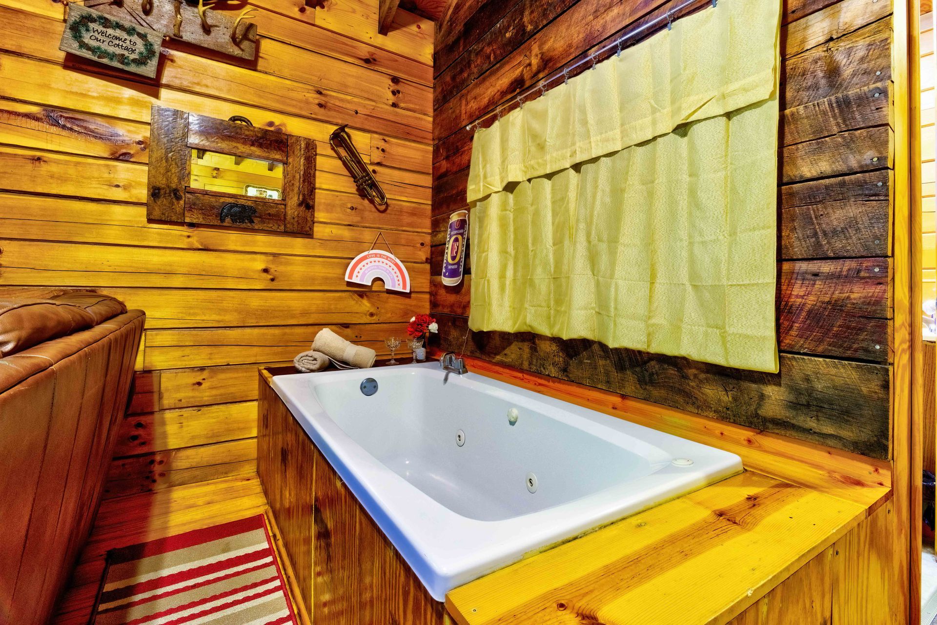 Rustic wood-paneled bathroom with a white bathtub, yellow counter, and curtained window
