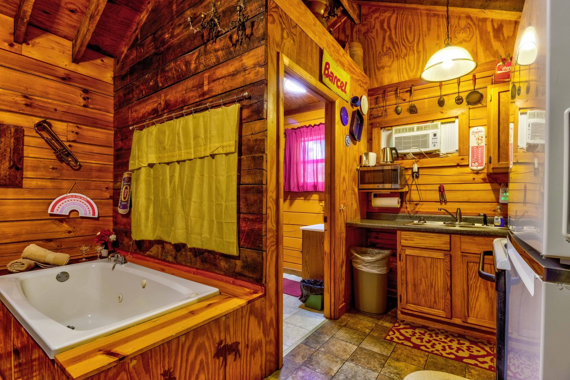 Rustic log cabin bathroom with a white sink, wooden cabinets, and a small kitchen area in warm lighting