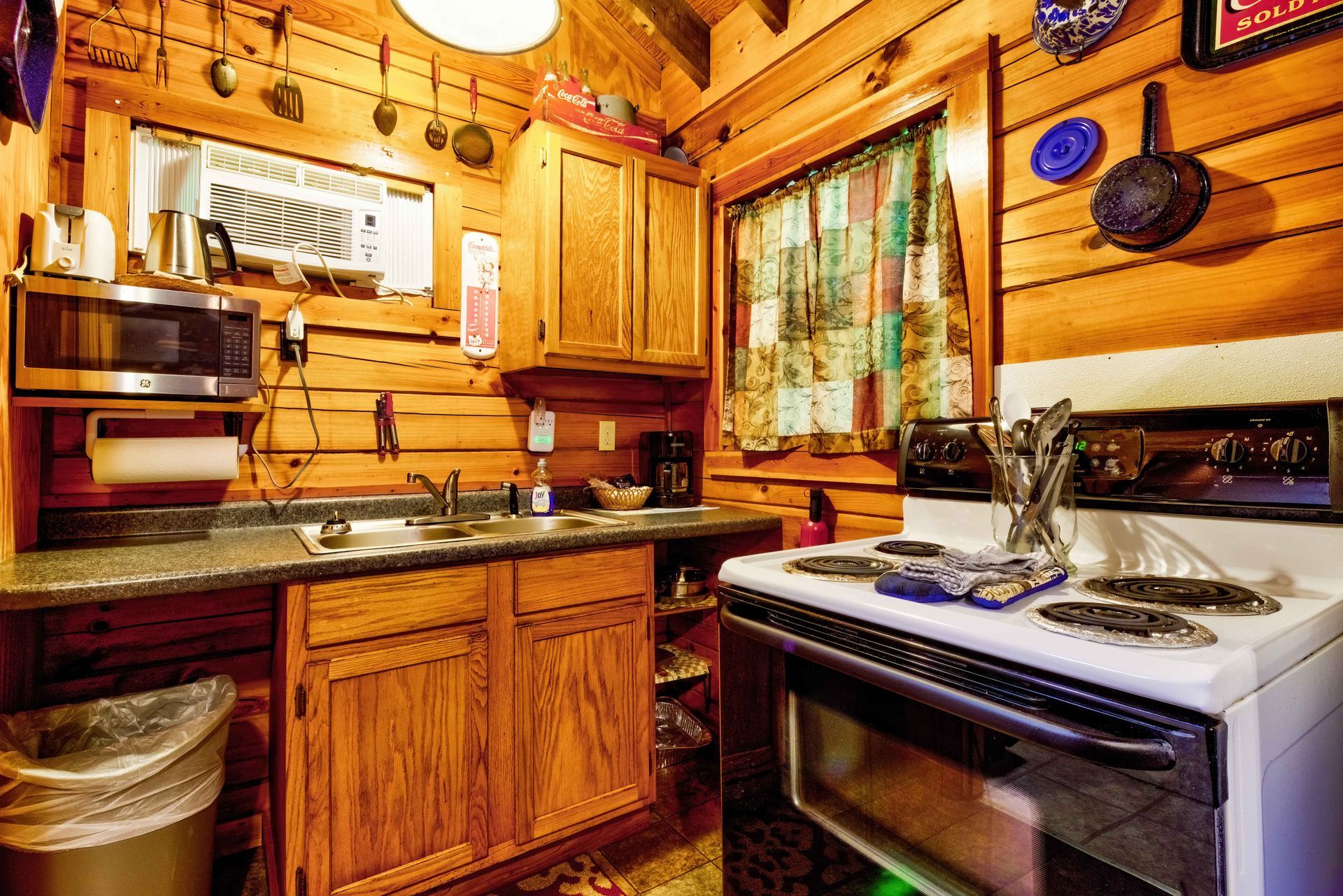 Cozy wood-paneled kitchen with stove, cabinets, sink, and hanging pots under warm lighting