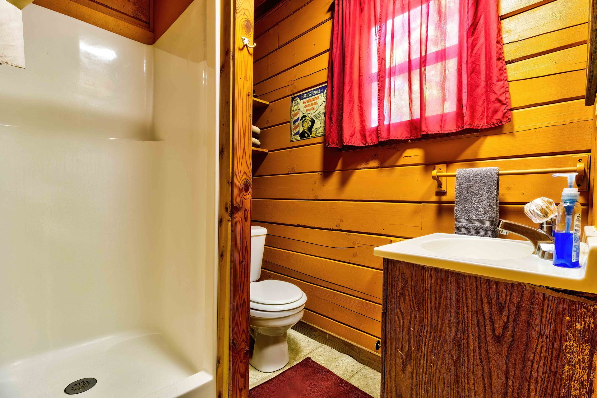 Small bathroom with a shower, toilet, and wooden vanity under a red curtain.