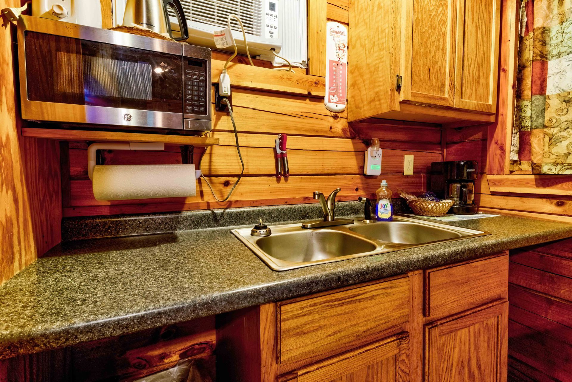 Wooden kitchen with granite counter, double sink, microwave, and paper towel holder under cabinets