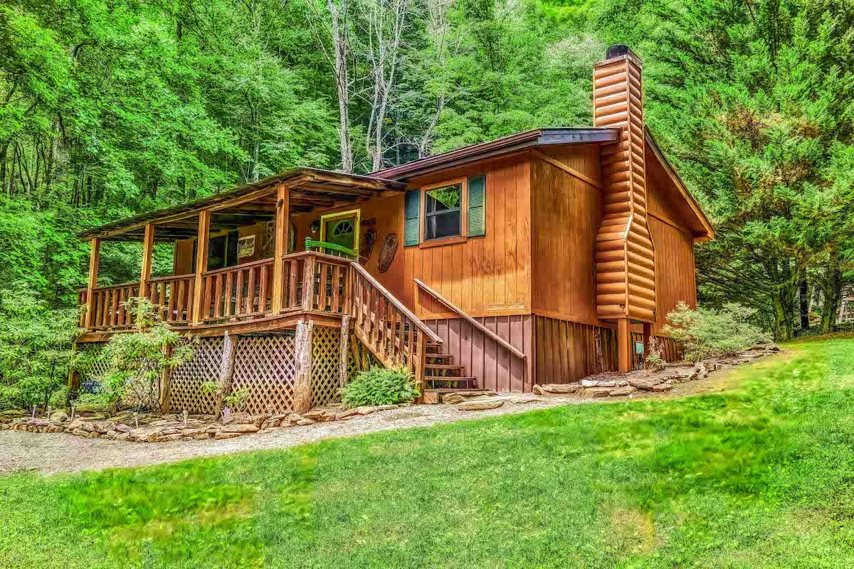 Wooden cabin with porch and stone chimney nestled in a lush green forest