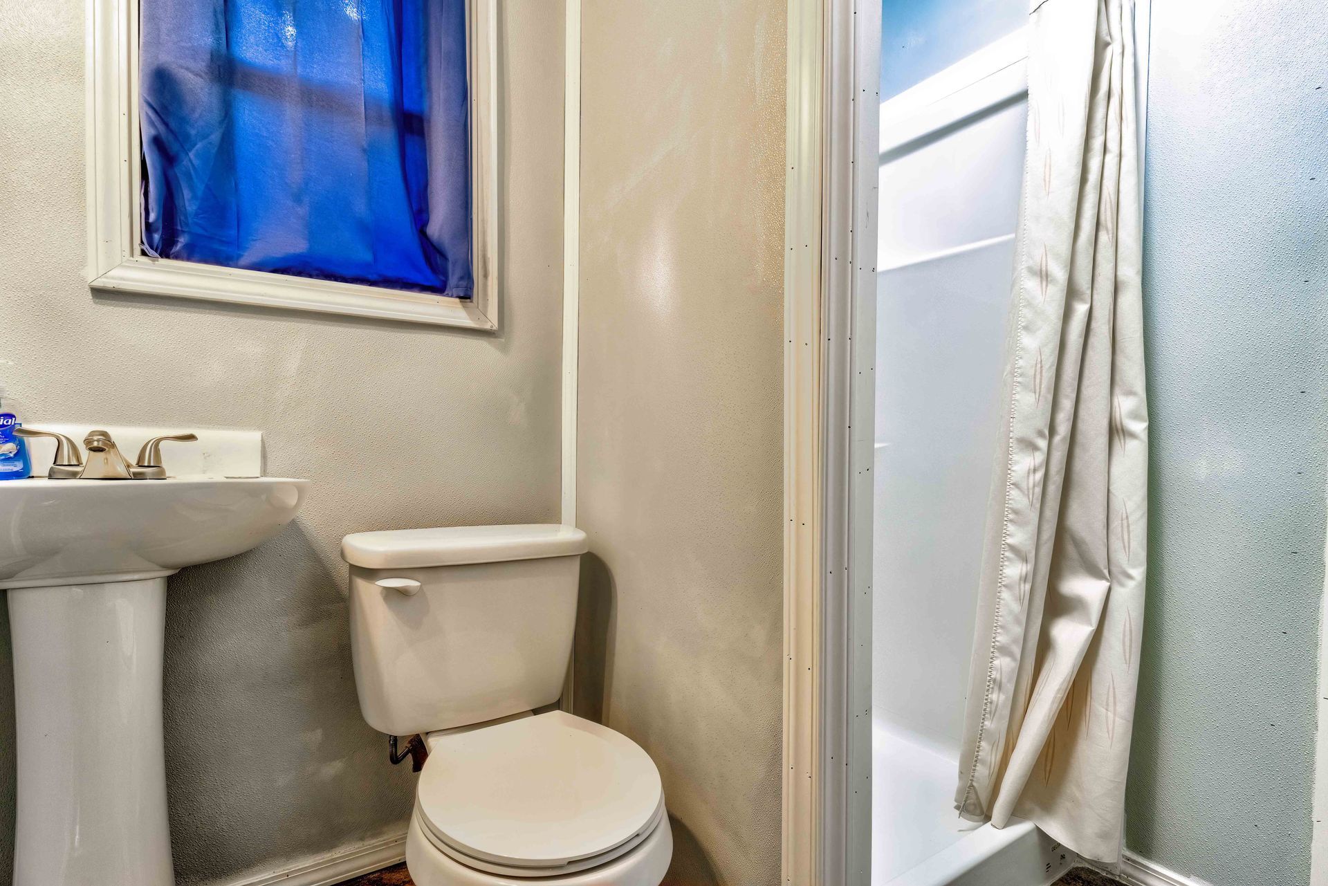 Small bathroom with a sink, toilet, and shower stall beside a frosted window.