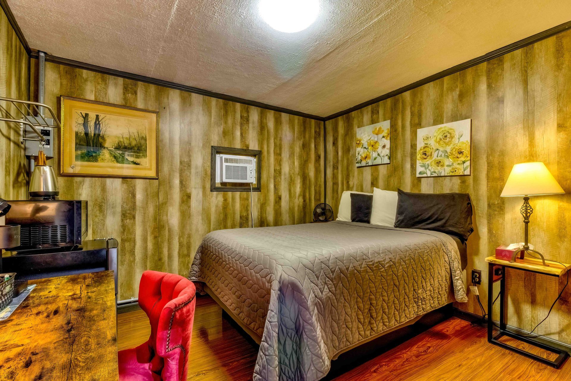 Cozy bedroom with a bed, bedside lamp, wood-paneled walls, and framed art.