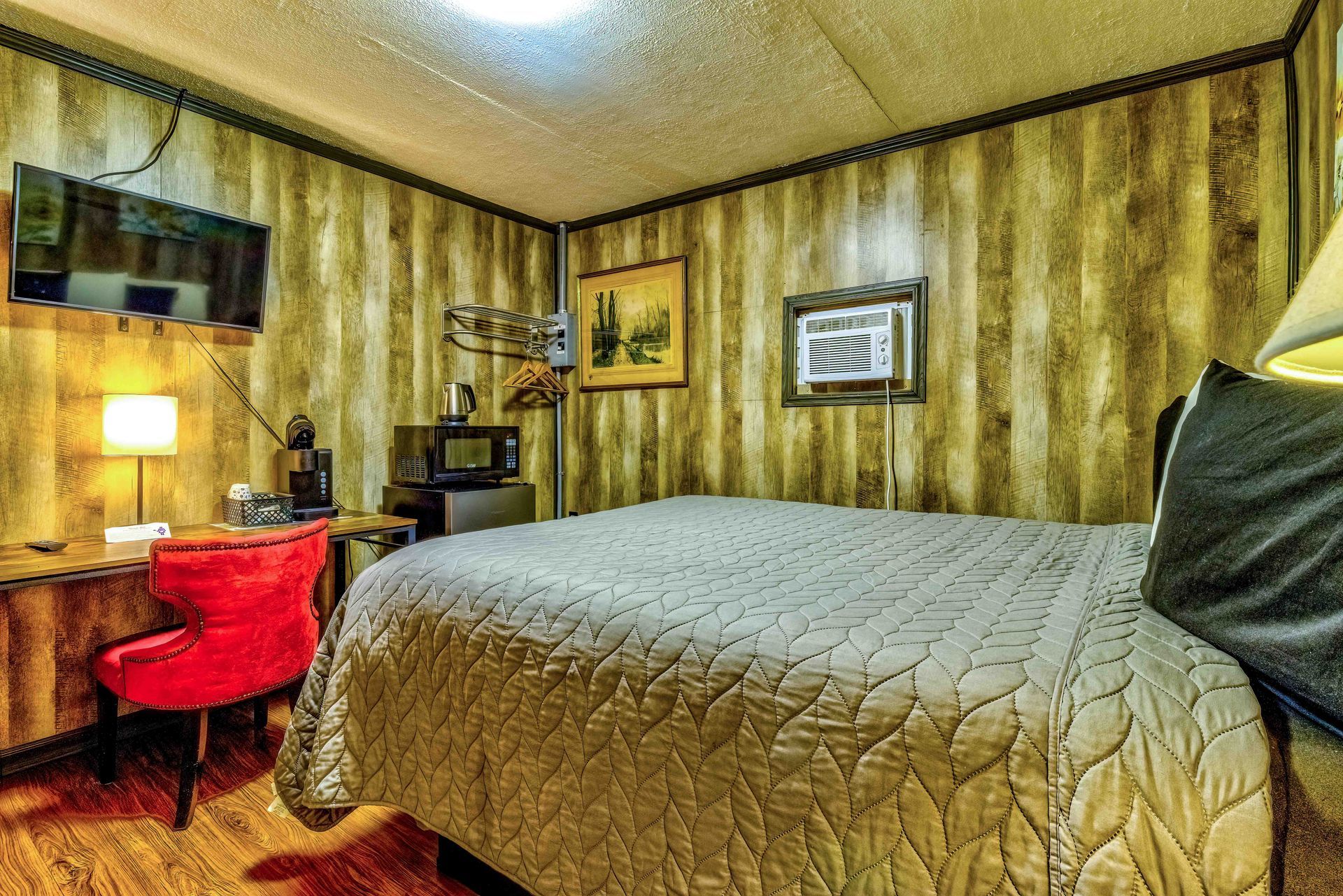 Hotel room with queen bed, red chair, desk lamp, and wood-paneled walls