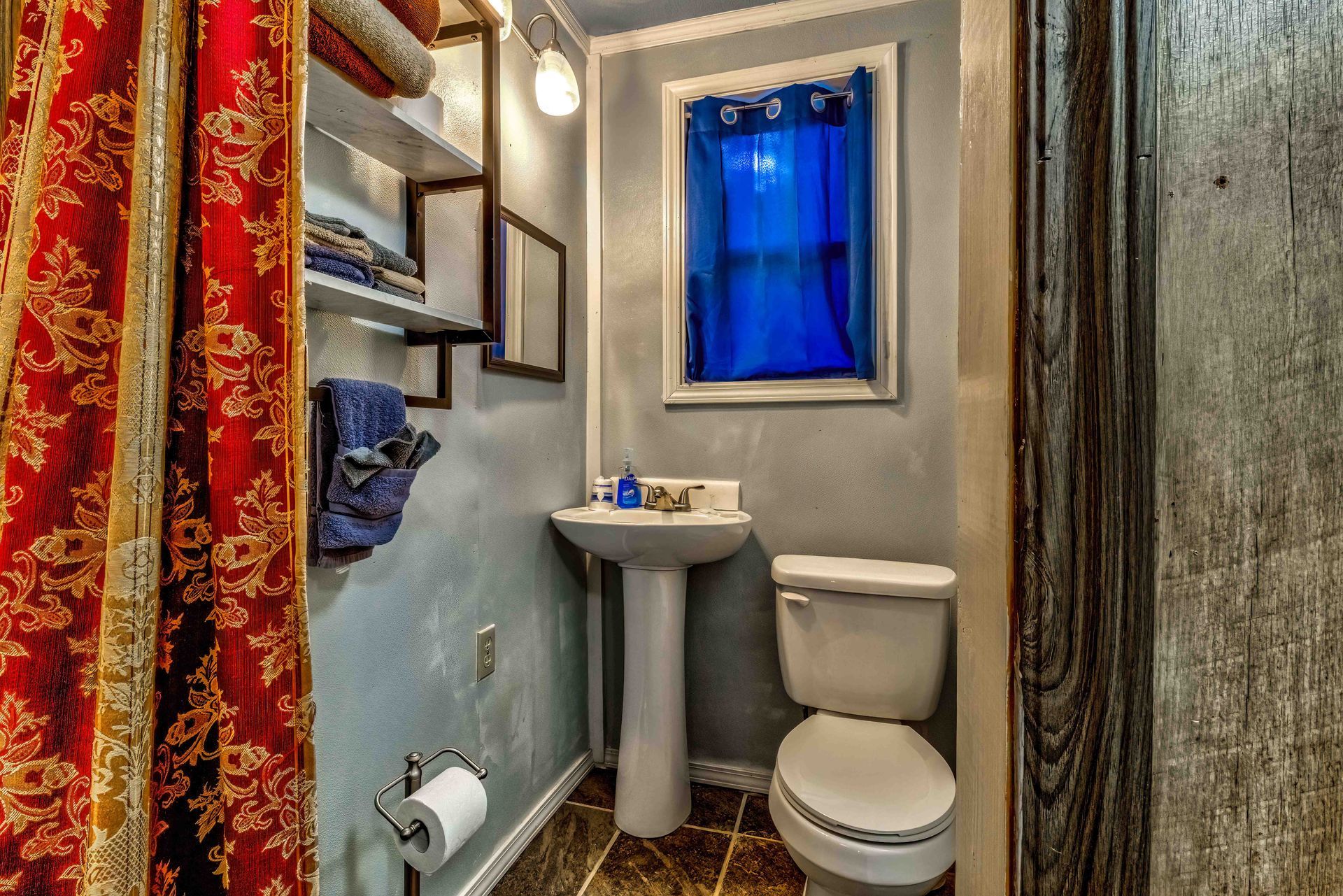 Small bathroom with pedestal sink, toilet, blue window, and red shower curtain
