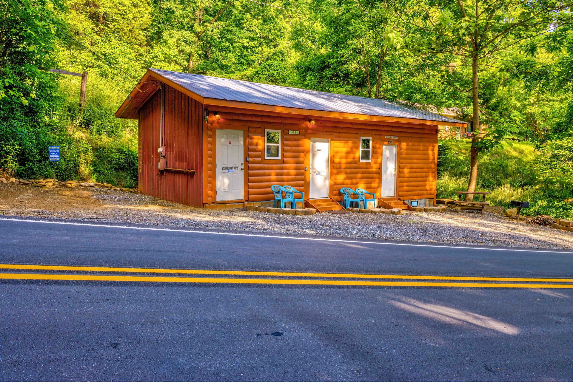 Small wooden roadside cabin with a solar-paneled roof, set beside a forest and empty road.