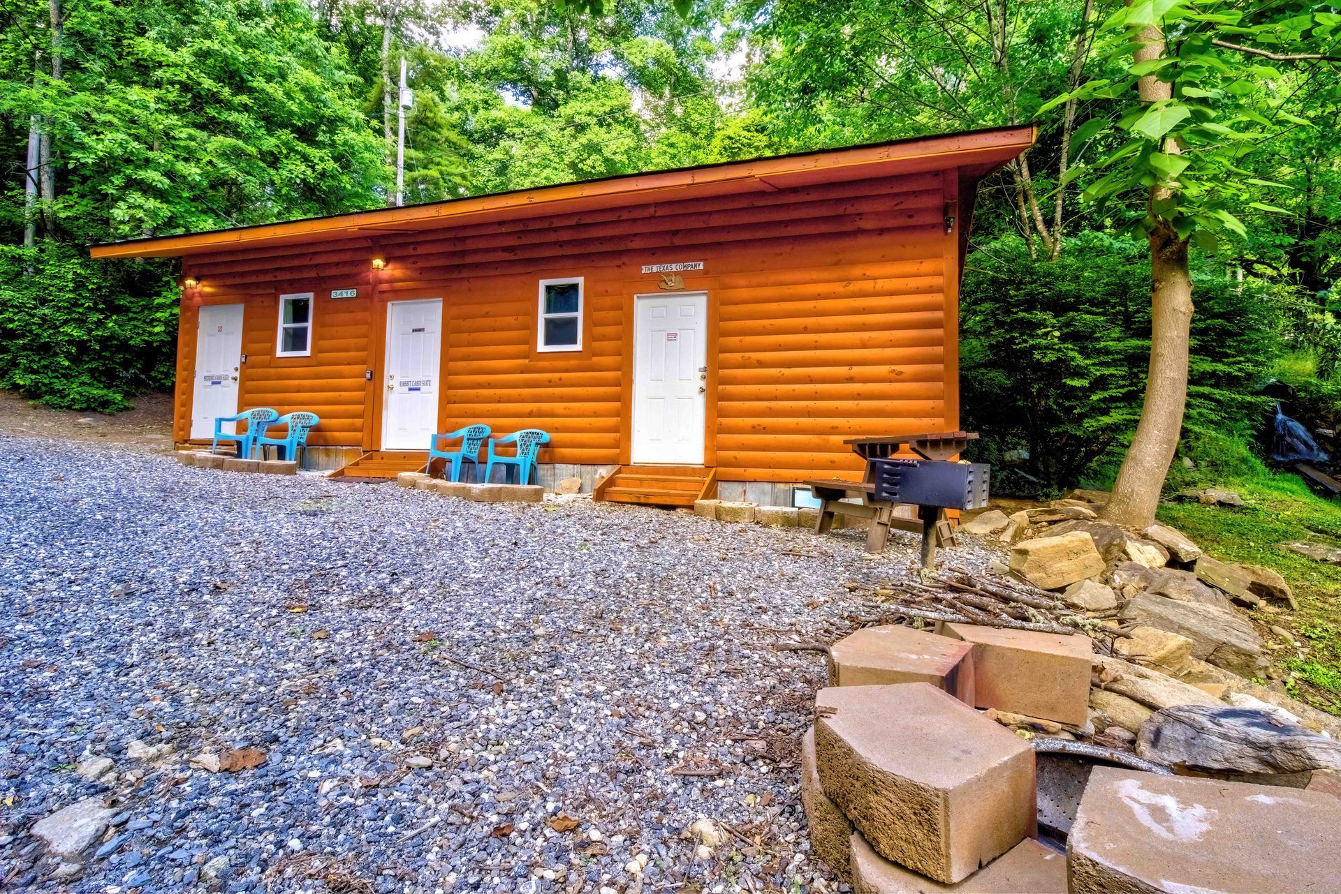 Rustic orange cabin with white doors and chairs on a gravel clearing surrounded by forest