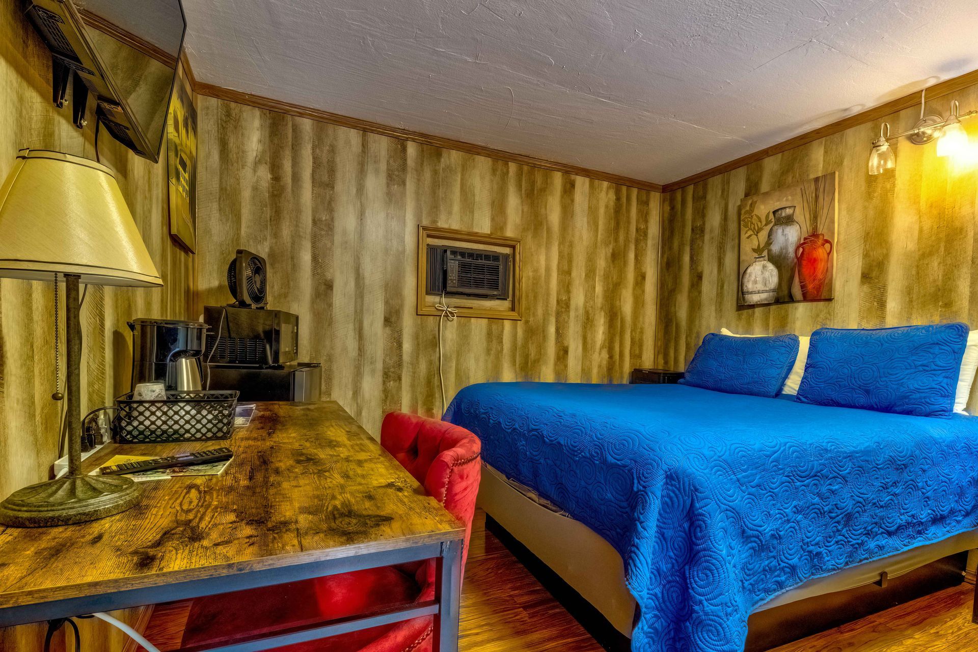 Cozy bedroom with blue bedspread, red chair, wooden desk, and warm yellow walls