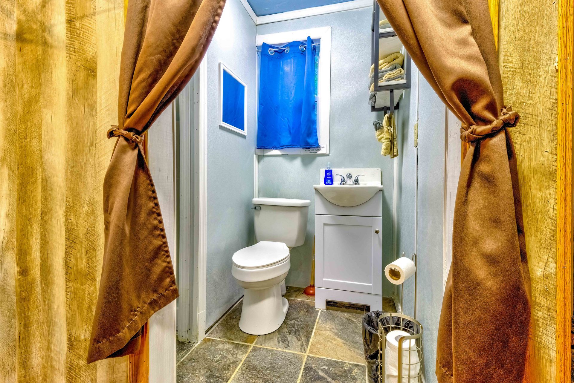 Small bathroom with toilet, sink, blue window curtain, and gold shower curtains