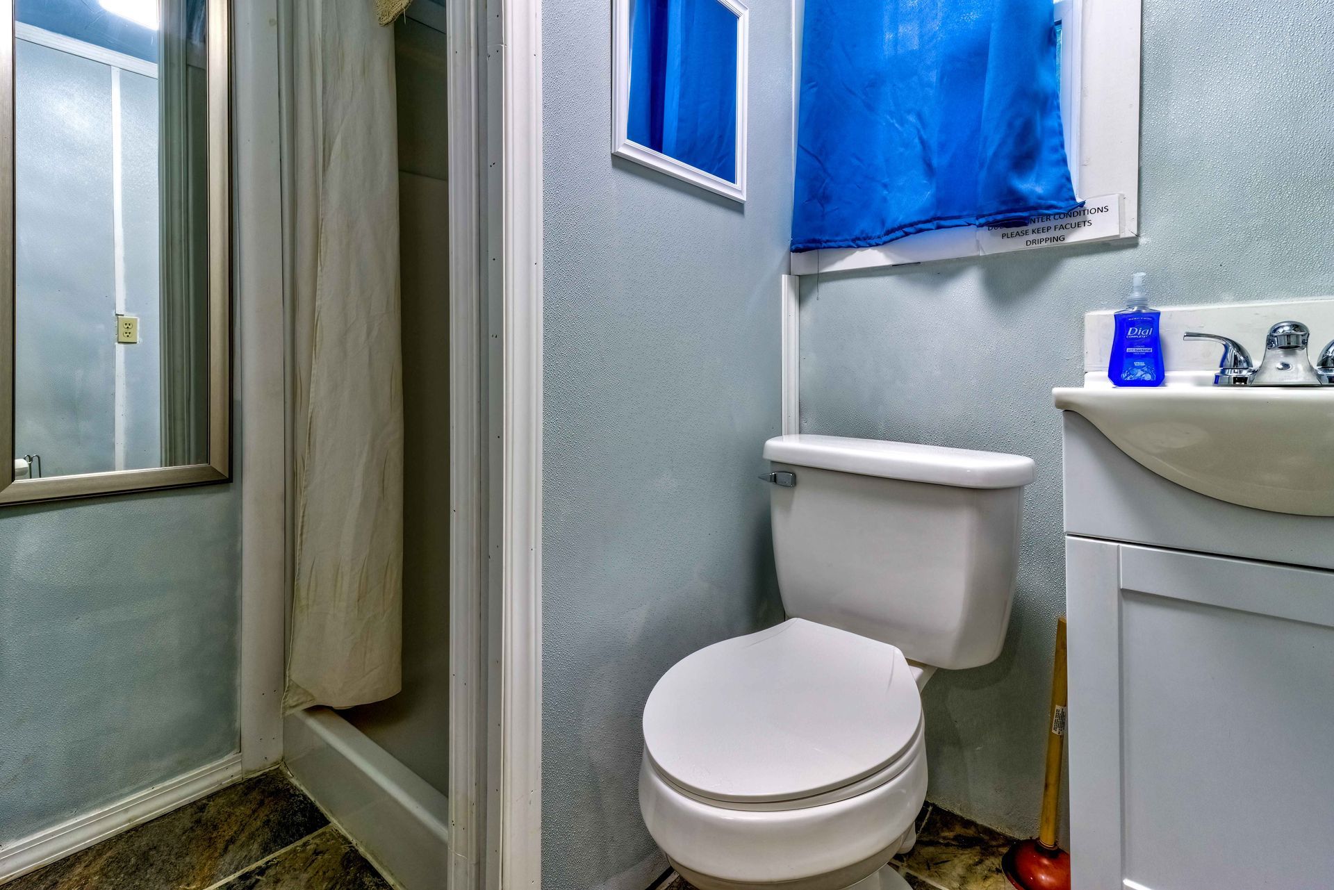 Small bathroom with toilet, shower curtain, and sink, featuring blue accents and a window.