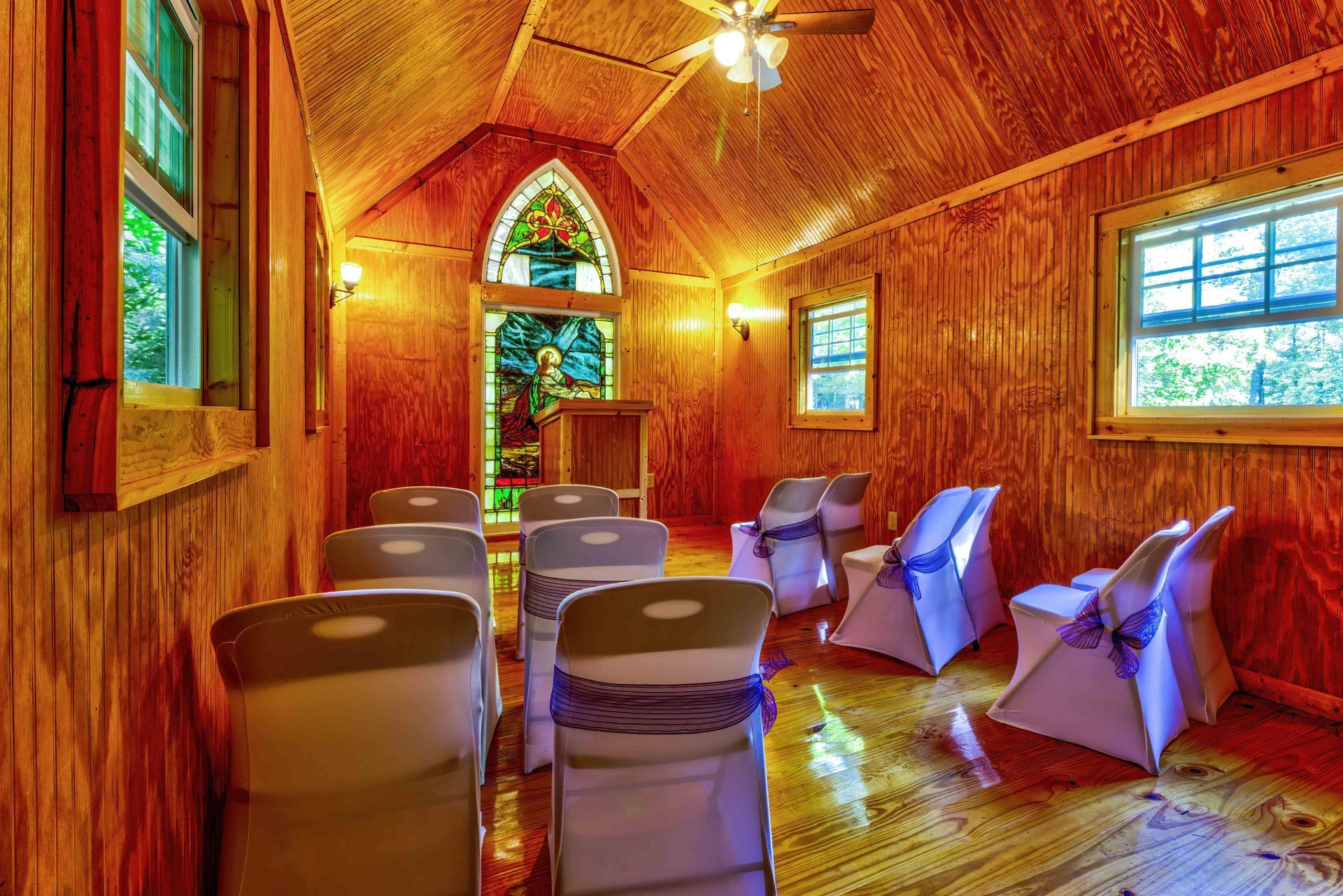 Wood-paneled chapel with white chairs, stained-glass windows, and a lectern at the front