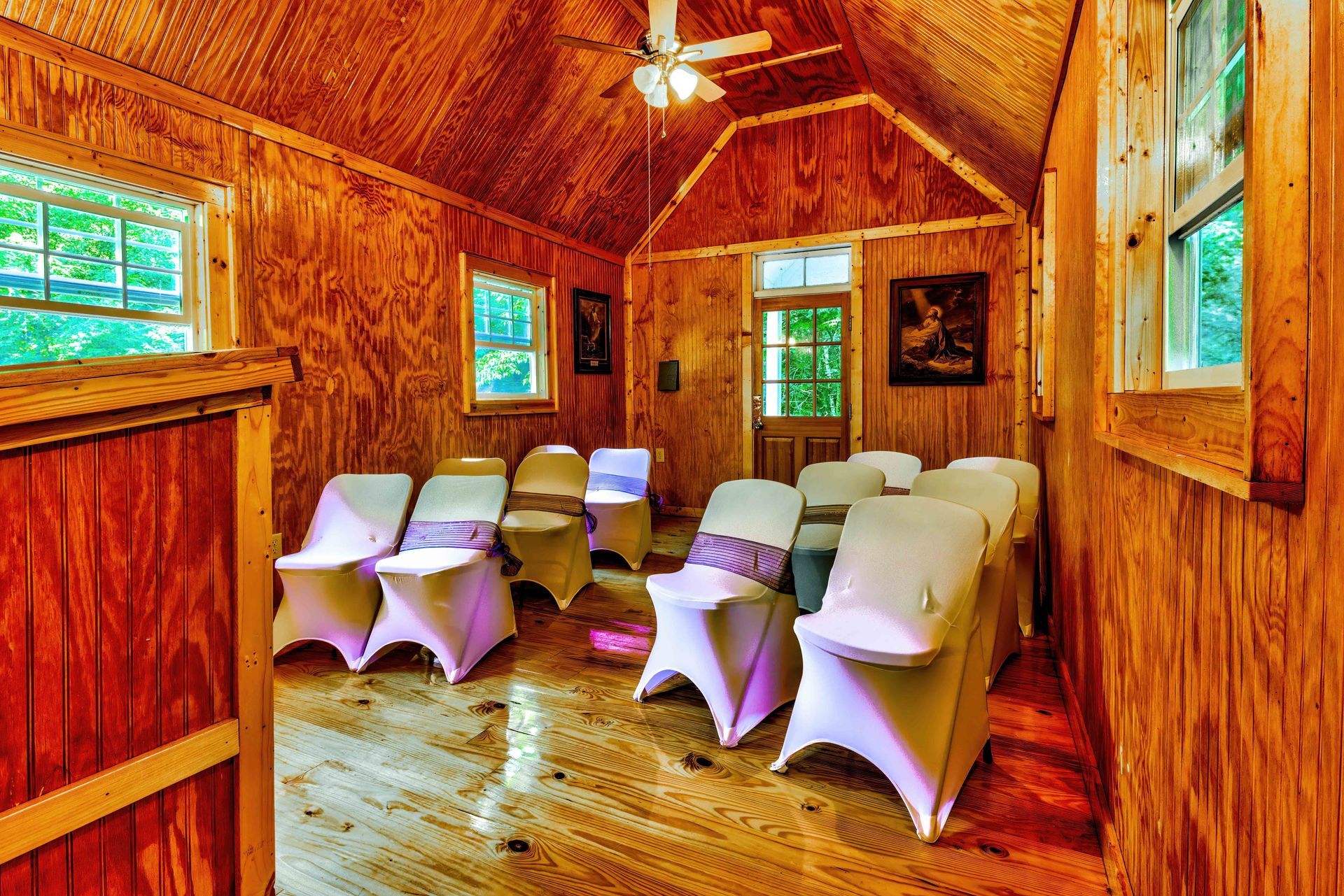 Wooden cabin room with white-covered chairs arranged in rows for a small meeting or ceremony