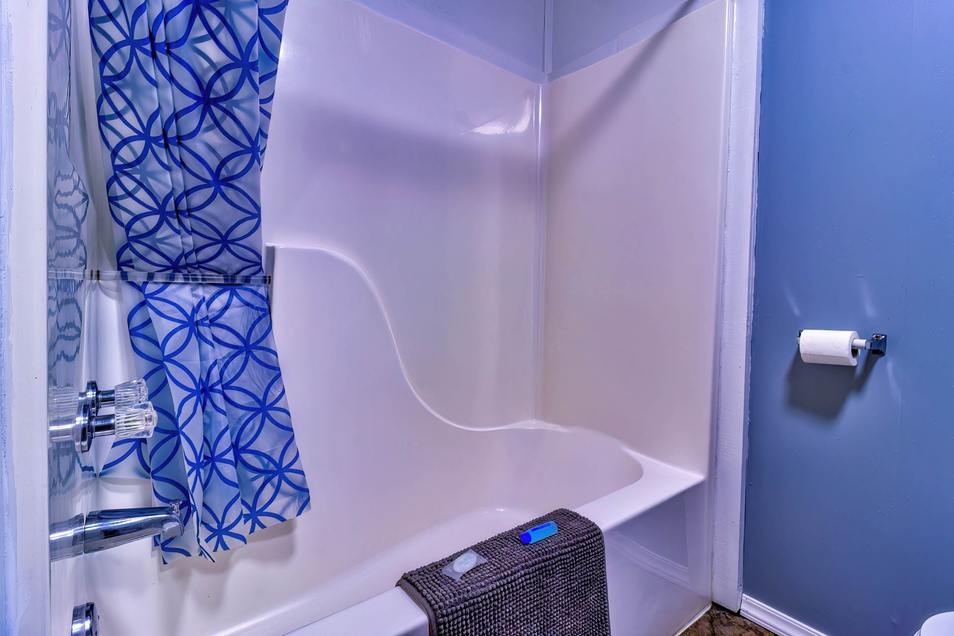 Bathroom with blue floral shower curtain, white tub, and patterned towel on the edge