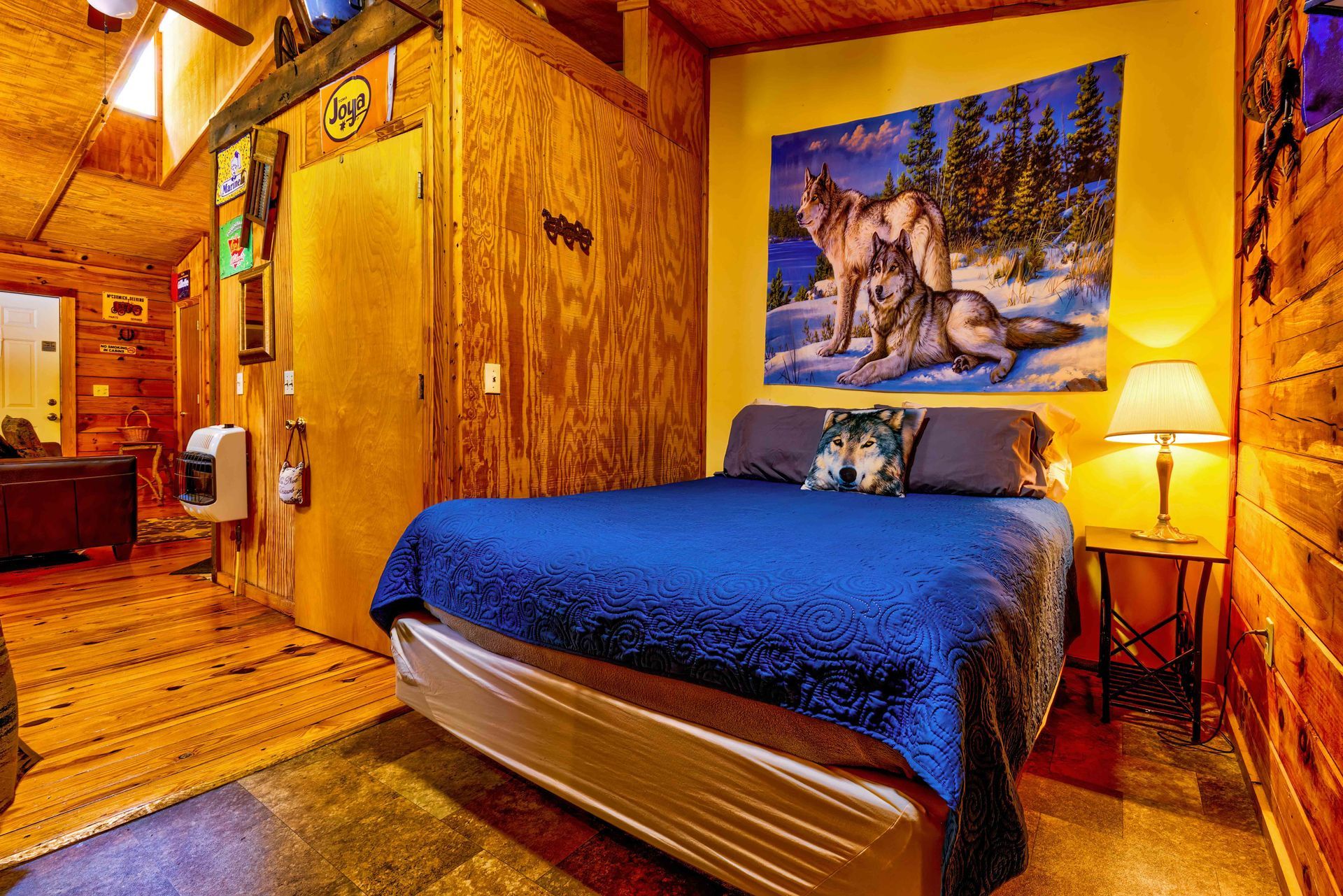 Rustic bedroom with blue bedspread, wolf wall art, warm wood walls, and a bedside lamp