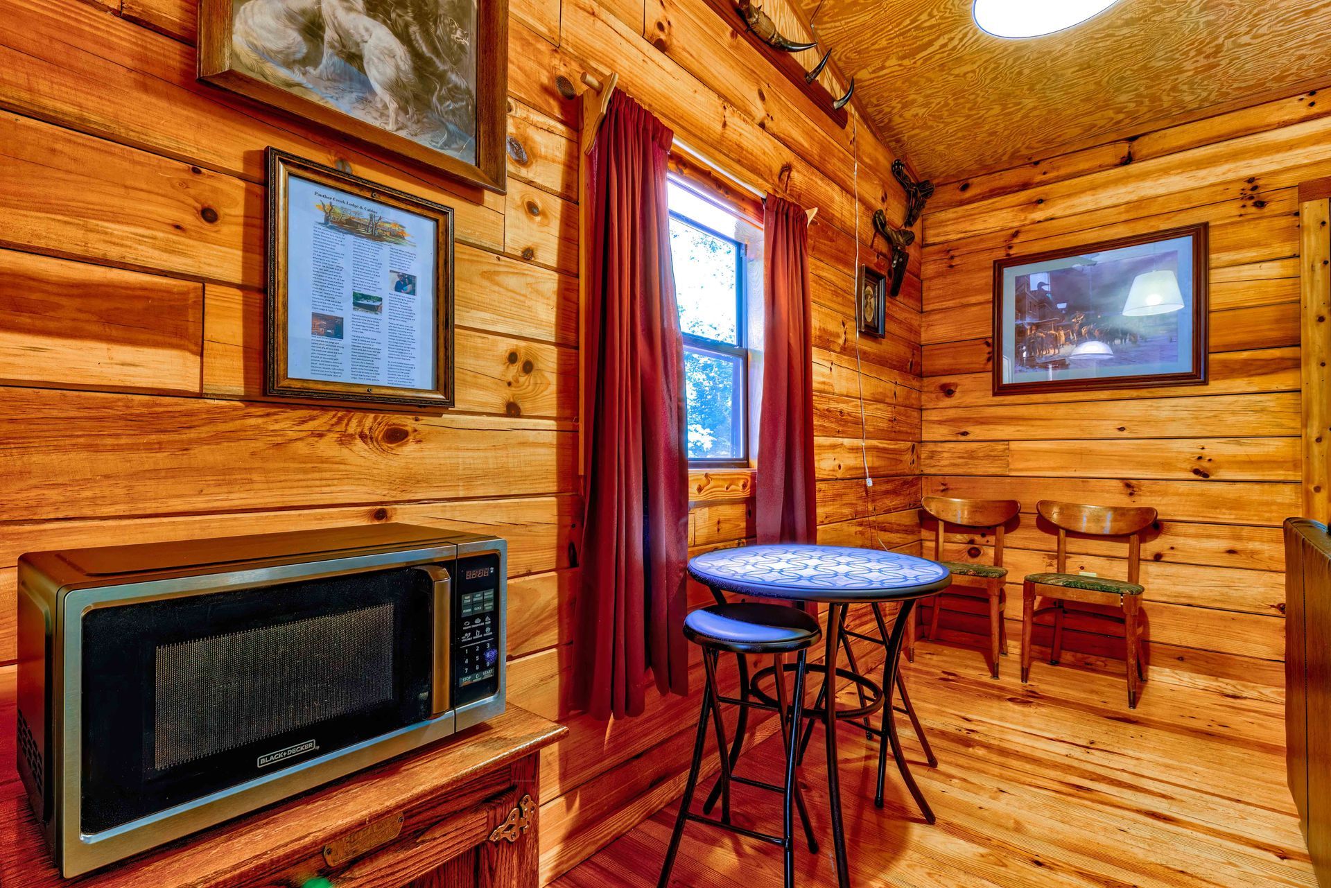 Cozy log cabin room with wood walls, table, chair, framed art, and a wall-mounted TV