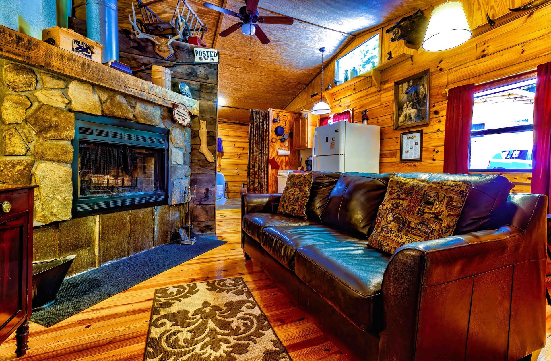 Rustic cabin living room with leather sofa, stone fireplace, wood walls, and warm lighting