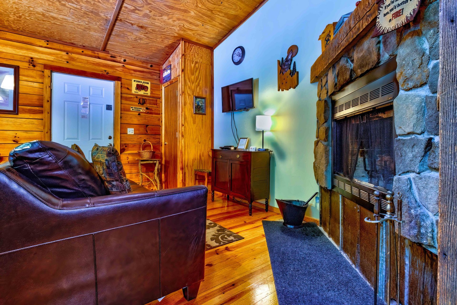 Cozy rustic living room with wood walls, leather chair, stone fireplace, and blue rug