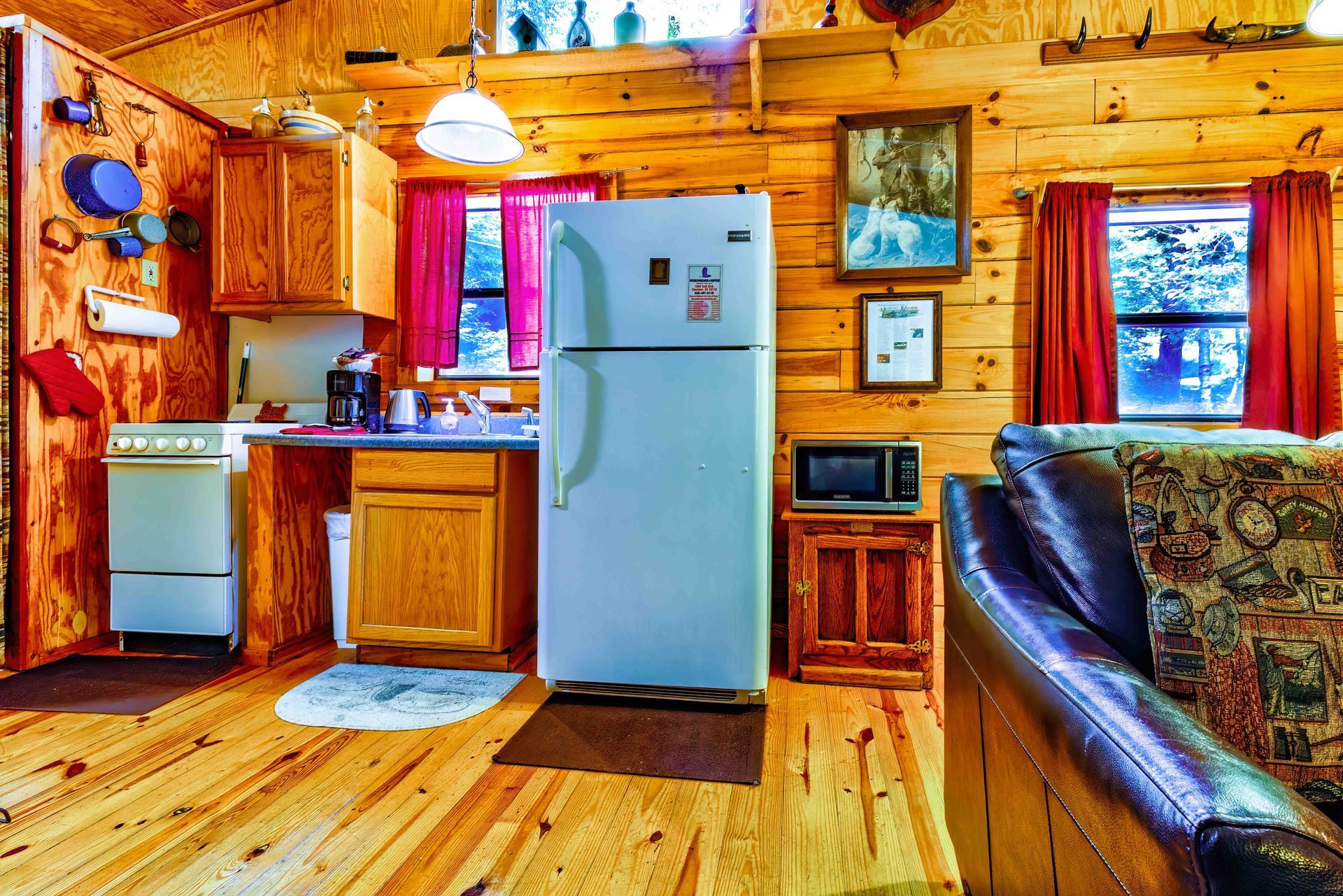 Cozy log cabin kitchen with wood cabinets, white fridge, and black leather couch by a window.