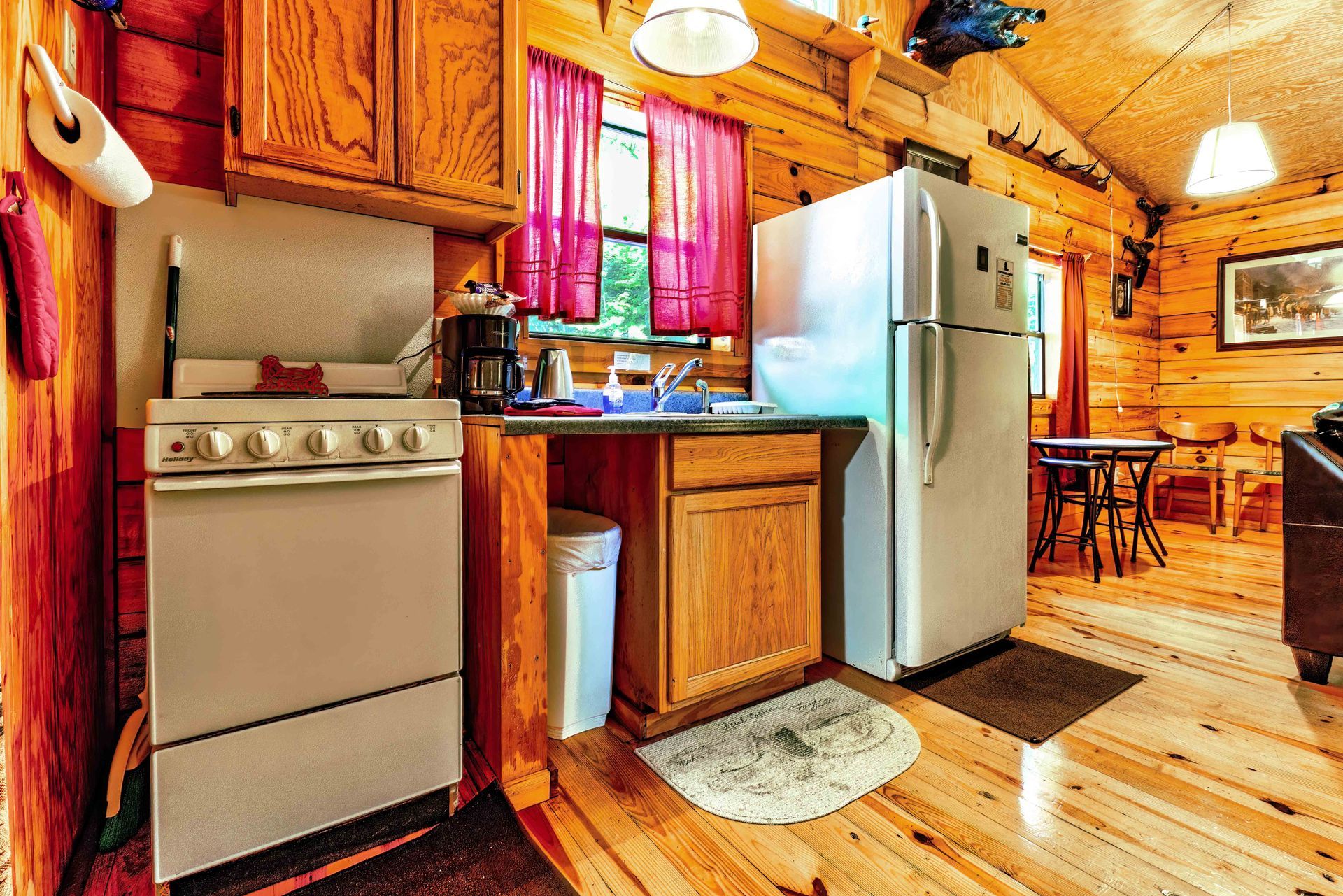 Cozy rustic kitchen with wooden cabinets, stainless appliances, and a red window curtain