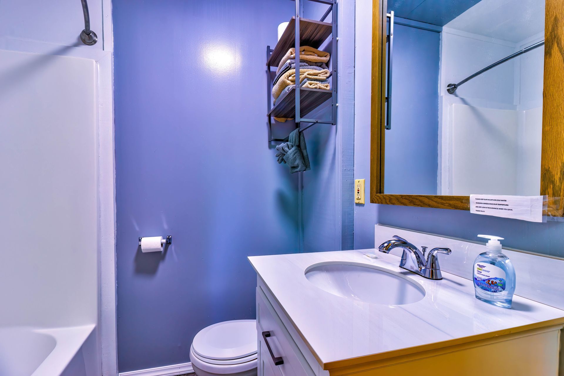 Small bathroom with blue walls, white tub, toilet, sink, and a mirror above the vanity.