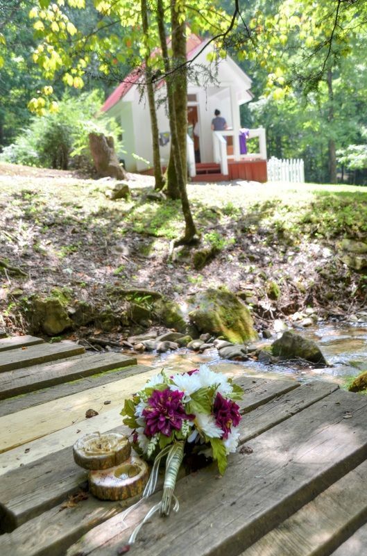 Bouquet and two gold containers on wooden planks by a creek, with a small white chapel in the background.