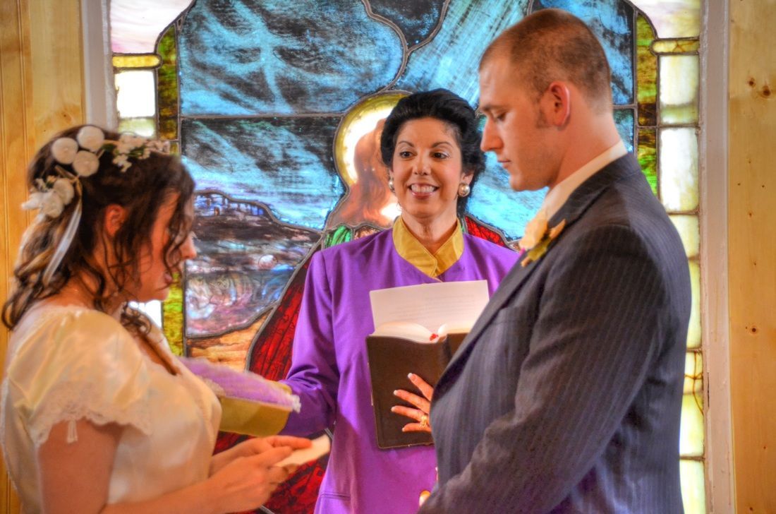 Wedding couple holding hands with officiant before a stained-glass window