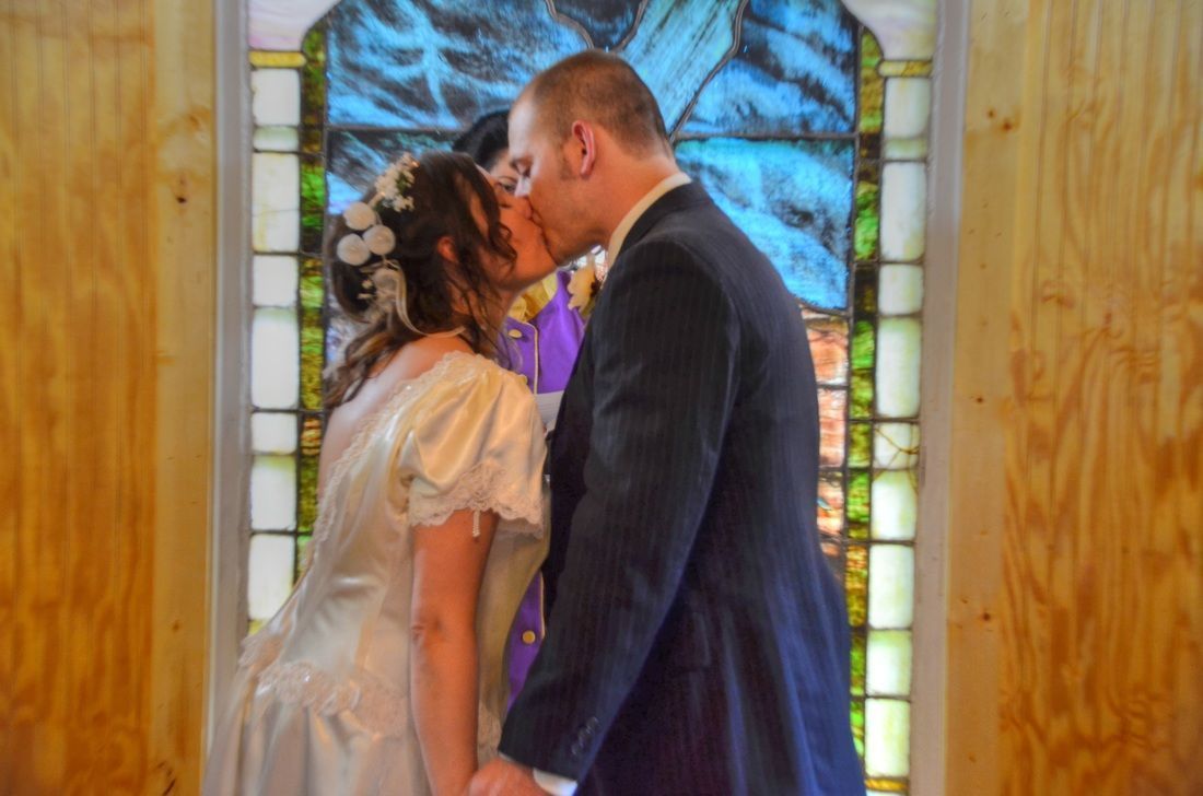 Couple kissing in front of a stained-glass window at a wedding ceremony