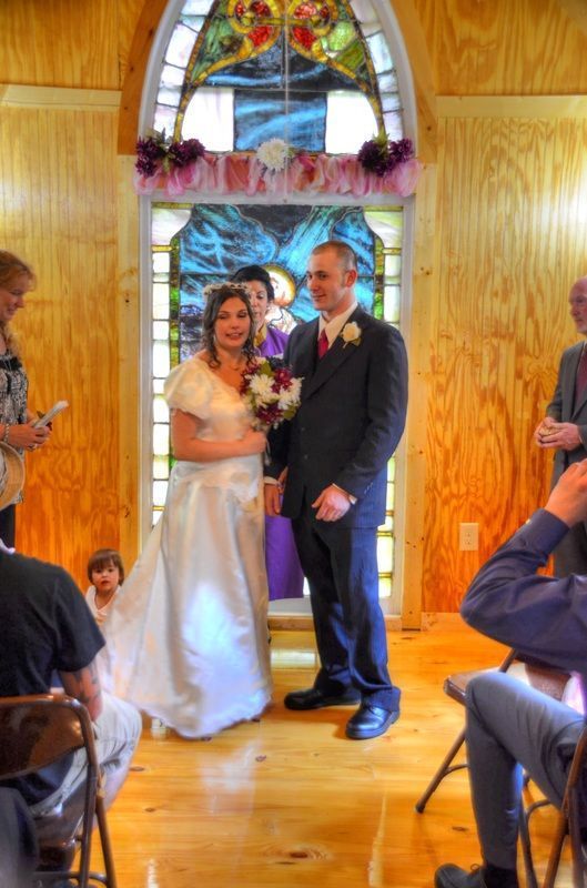 Bride and groom standing in a wooden chapel doorway, holding hands and smiling during a wedding ceremony