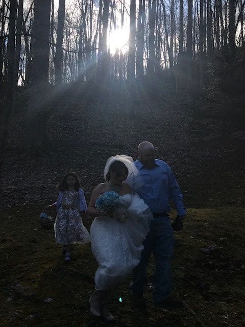 Three people walking in a dark wooded area at sunset, with sunbeams filtering through the trees.