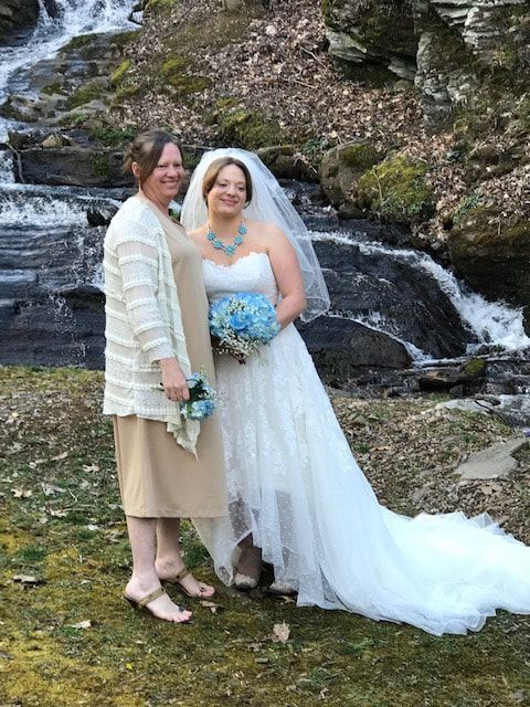 Two people in formal attire posing by a small waterfall in a rocky outdoor setting