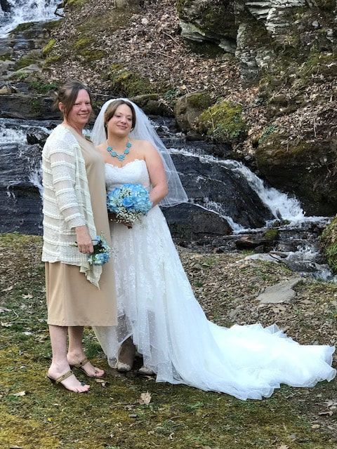 Two people posing in wedding attire beside a small waterfall in a rocky, mossy outdoor setting
