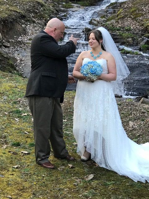 Bride and man standing by a waterfall, exchanging a heartfelt moment outdoors