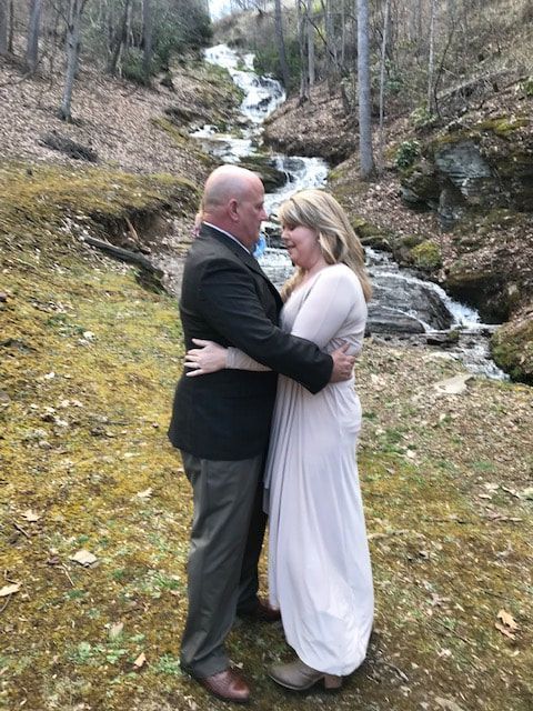 Couple embracing by a small waterfall in a wooded outdoor setting
