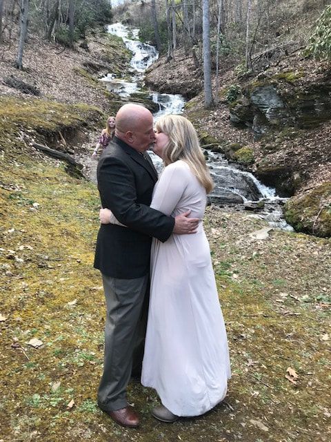 Couple embracing outdoors by a small waterfall in a wooded setting