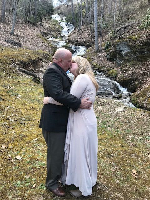Couple embracing on a mossy hillside beside a small waterfall in a forest