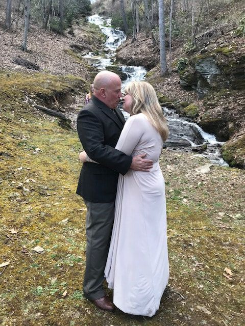 Couple embracing beside a small waterfall in a wooded outdoor setting