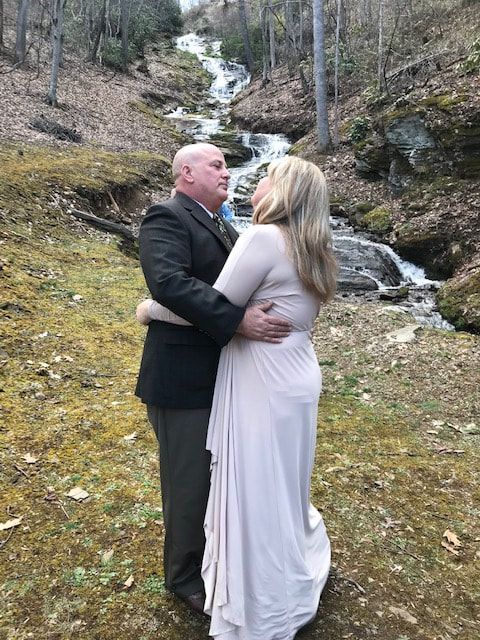 Couple embracing beside a small waterfall in a wooded outdoor setting