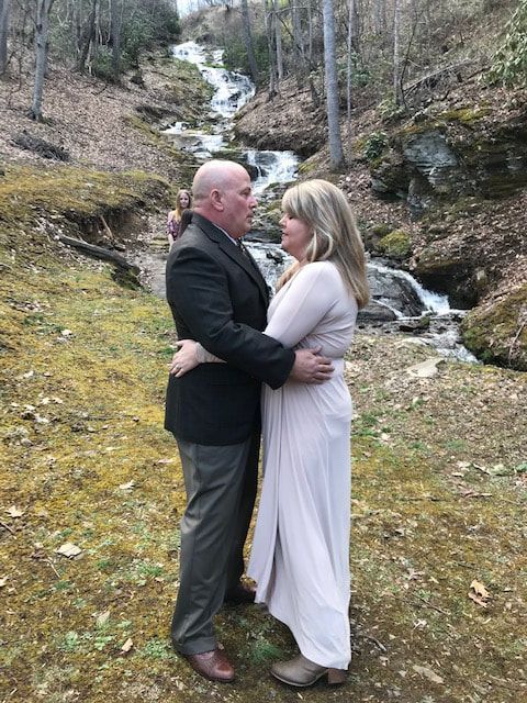 Couple embracing outdoors beside a wooded stream and small waterfall
