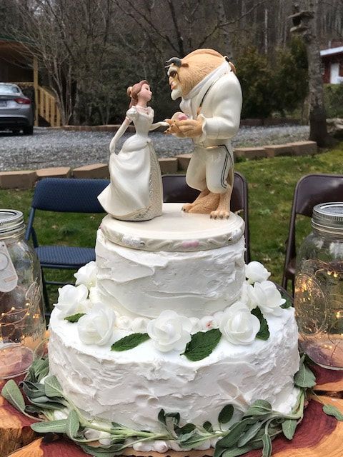 Wedding cake topper of a bride and groom dancing on a white tiered cake with flowers