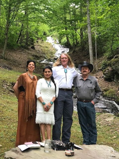 Four people posing in hiking clothes beside a forest waterfall and rocky stream.