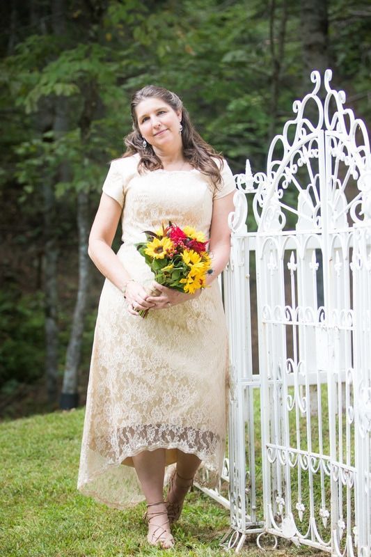 Woman in a cream lace dress holding a colorful bouquet beside a white garden gate.