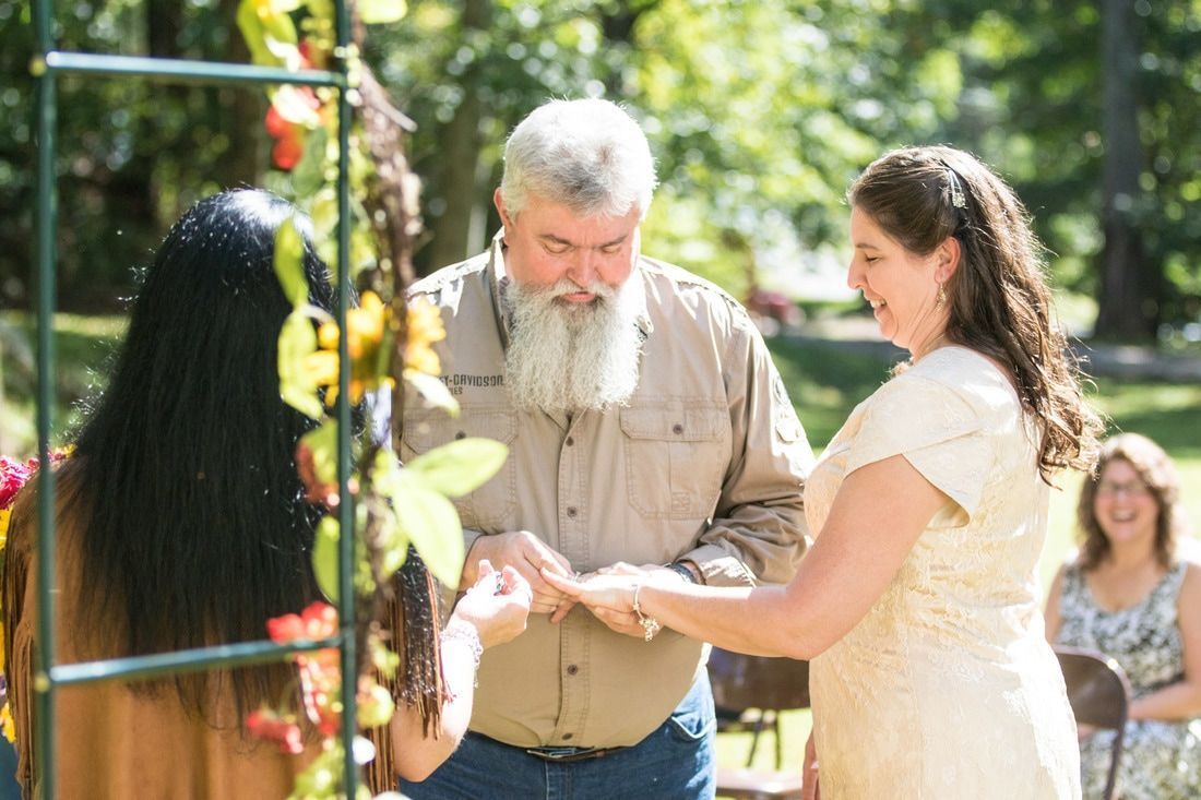 Man and woman exchanging rings outdoors at a sunlit garden ceremony